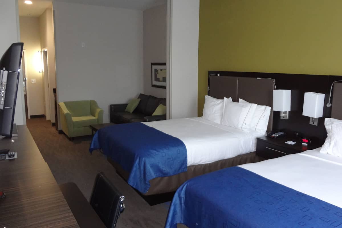 A hotel room with two beds, a desk, a chair, and a television.
