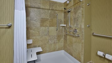 Een moderne badkamer met douche, handgrepen, een wit wastafel en een handdoekdispenser.