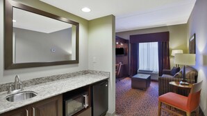 A hotel room with a kitchen area, a seating area with a sofa and armchair, and a large mirror. - Hampton Inn Brockport, NY (Brockport)