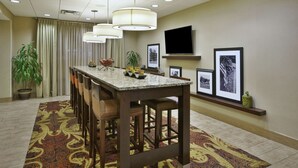 A hotel lobby with a long bar area, a flat-screen TV mounted on the wall, and a patterned carpet. - Hampton Inn Brockport, NY (Brockport)