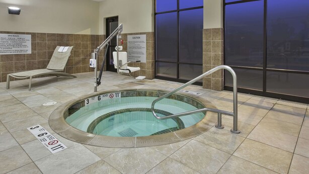 A spa area with a hot tub, safety signs, and a view of the city through large windows. - Hampton Inn Brockport, NY (Brockport)