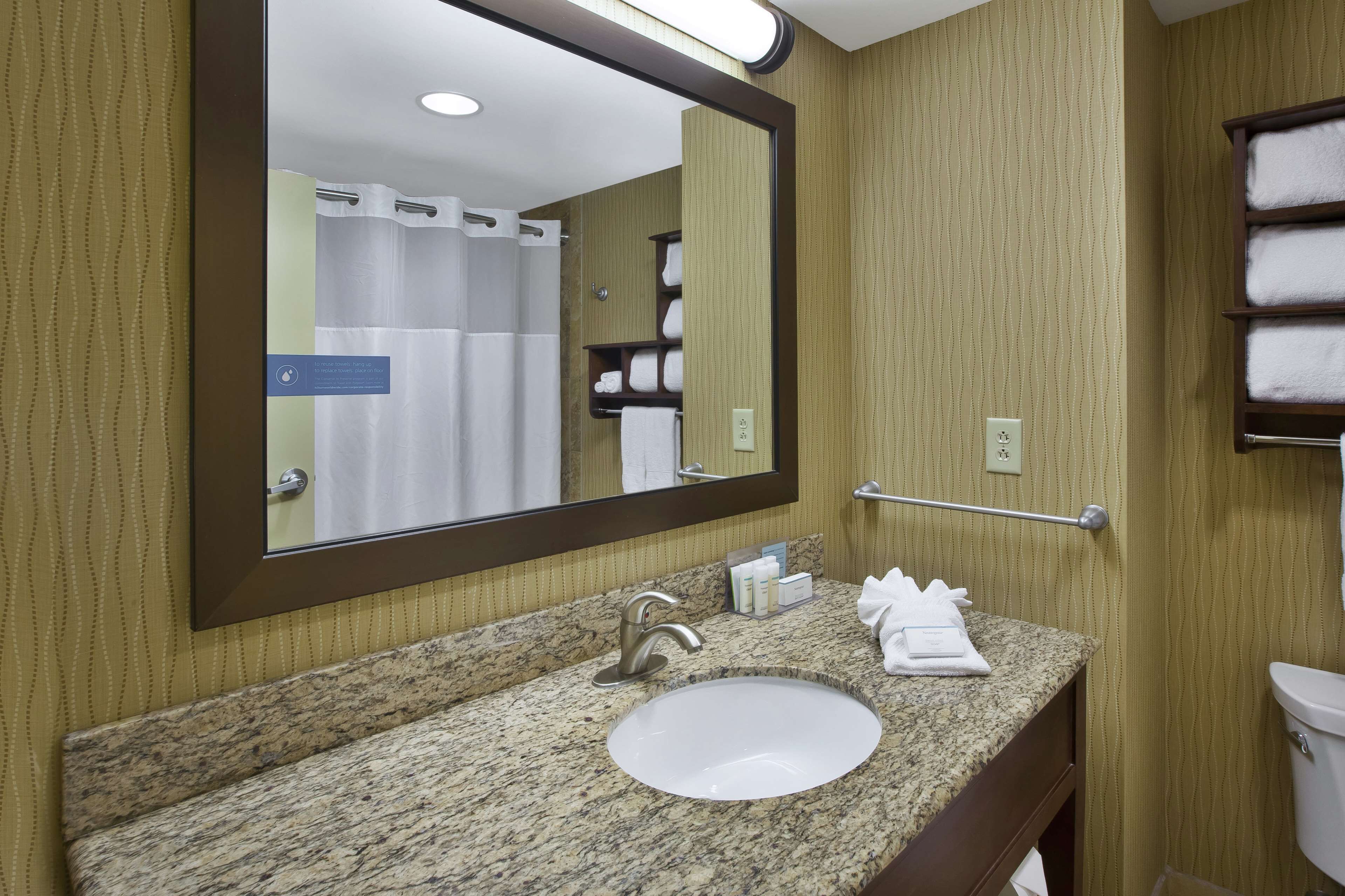 A bathroom with a granite countertop, a sink, a mirror, a towel rack, and a shower curtain.