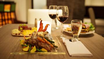 A dining table with a variety of dishes, including steak, vegetables, and a dessert. There are also two glasses of red wine and a water glass.