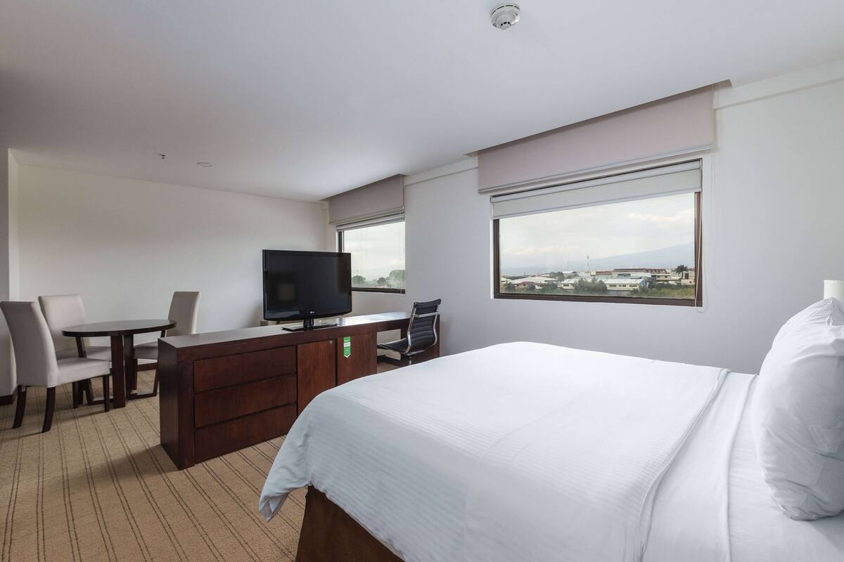 Een hotelkamer met een bed, een bureau, een stoel, een televisie en een raam met uitzicht op de stad.