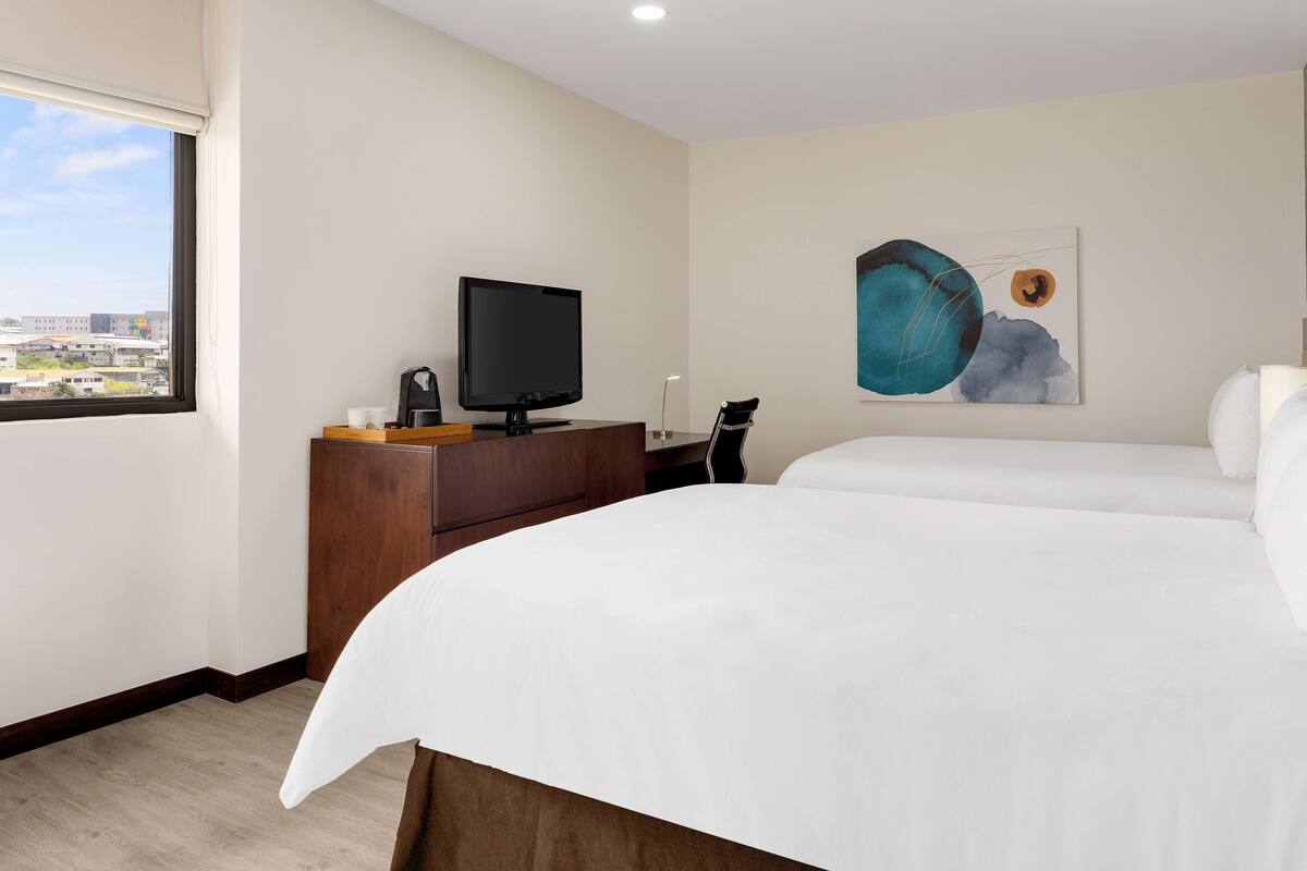 Een hotelkamer met een bed, een bureau met een televisie, een koffieapparaat en een schilderij aan de muur.