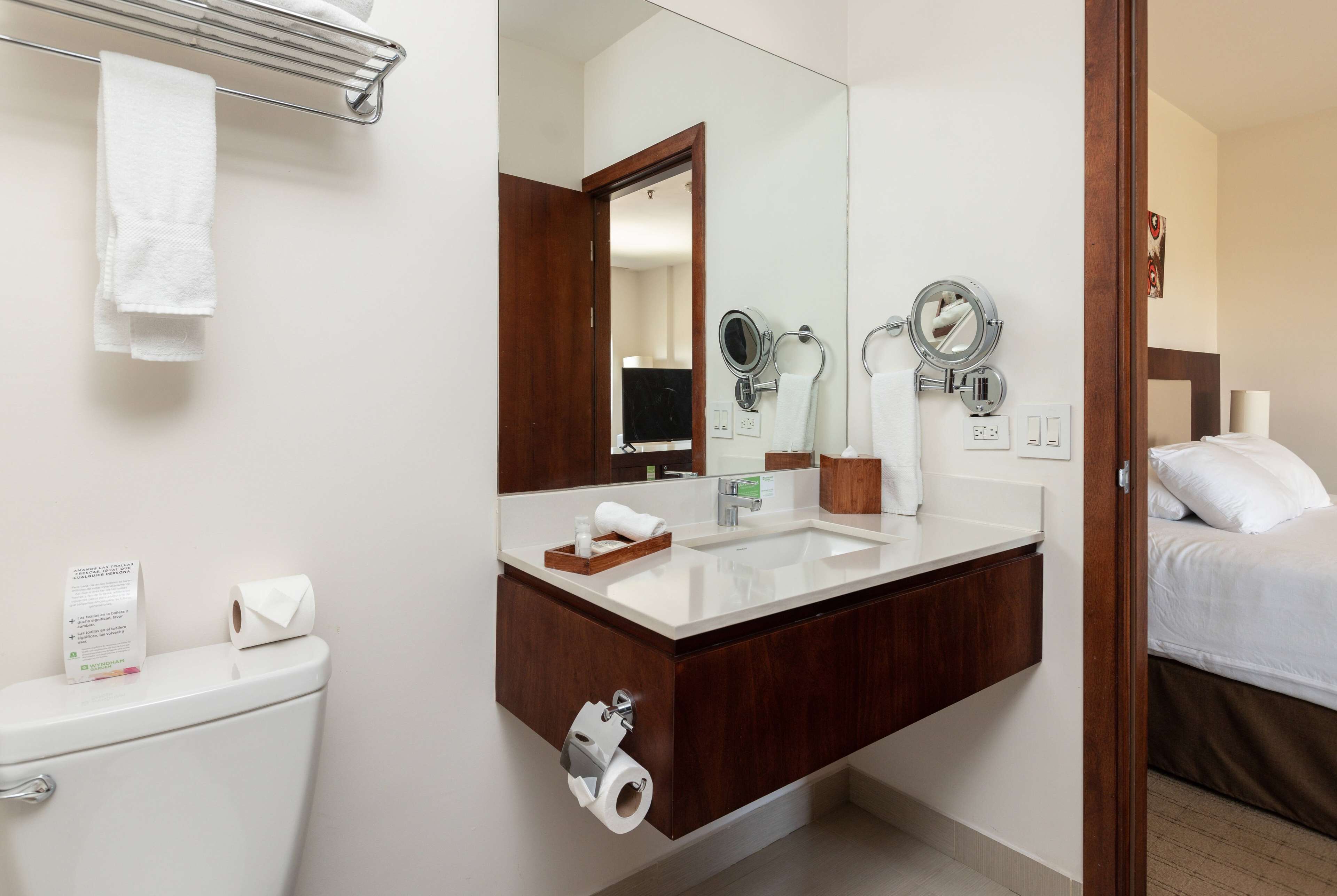 A hotel bathroom with a toilet, sink, and mirror.