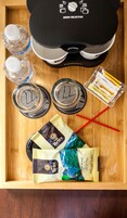 A wooden tray with a coffee maker, two water bottles, two glasses, and packets of coffee and tea.