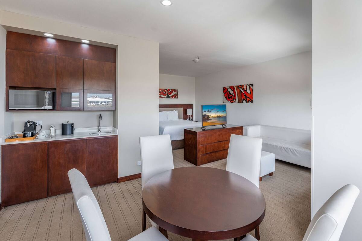 Een moderne hotelkamer met een kitchenette, een eettafel met stoelen, een bank en kunstwerken aan de wanden.