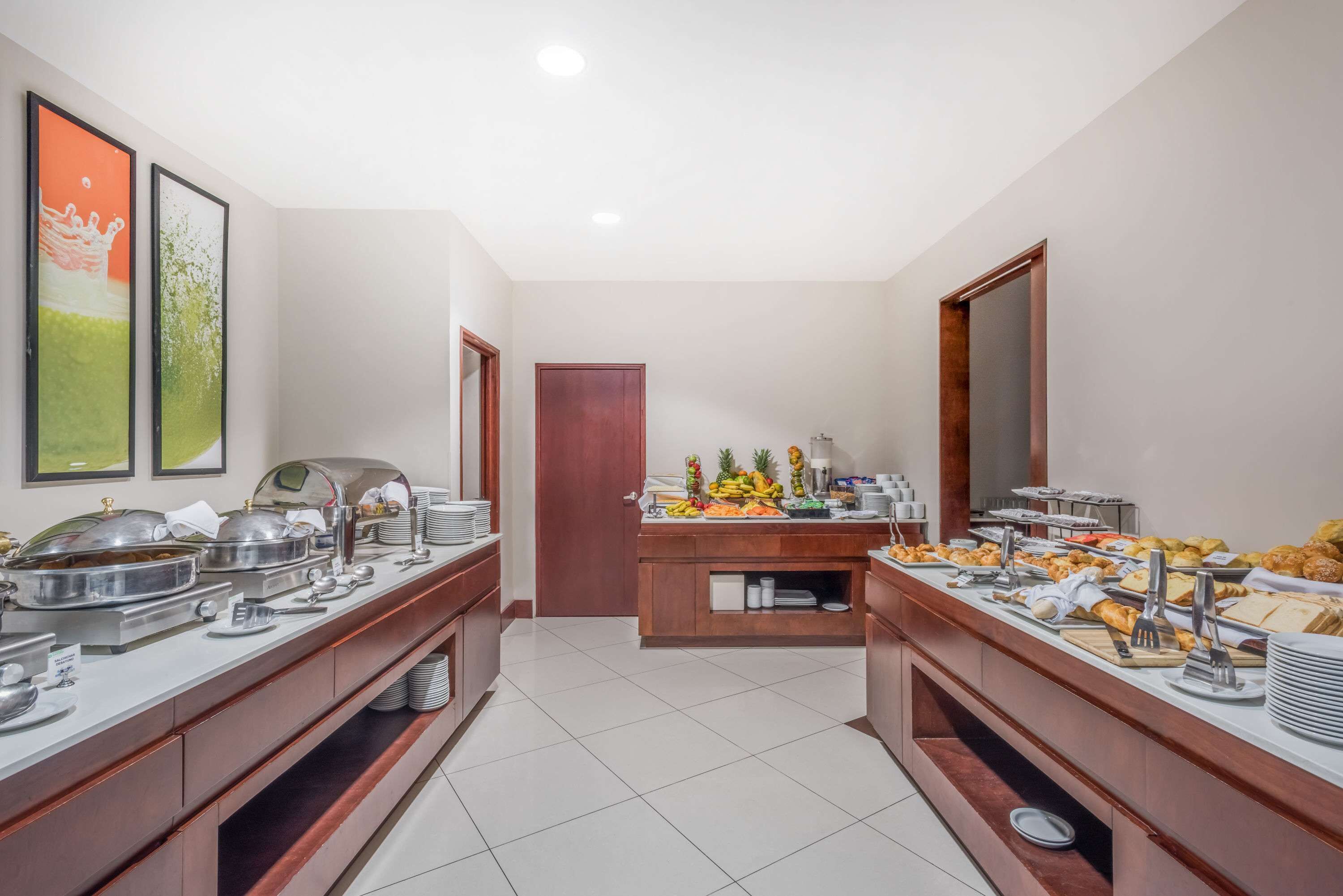 A buffet setup with multiple serving stations, including hot and cold food options, arranged in a spacious room with a tiled floor and wooden counters.