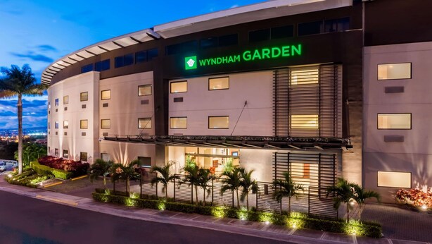 Un hotel moderno con una fachada curva, un llamativo letrero 'Wyndham Garden' y ventanas bien iluminadas.