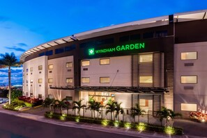 A modern hotel with a curved facade, a prominent 'Wyndham Garden' sign, and well-lit windows. - Wyndham Garden San Jose Escazu (San Rafael)