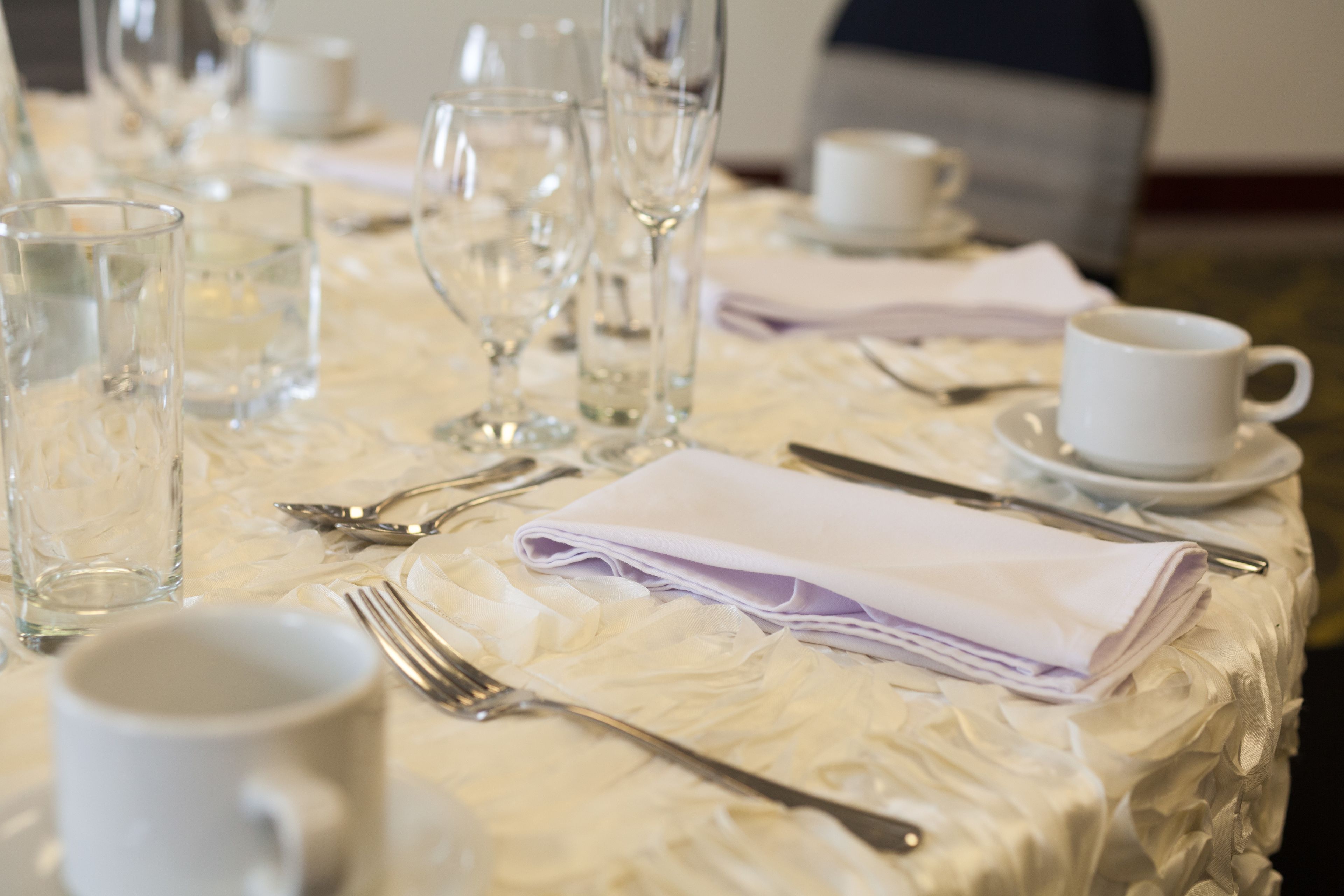 A table set with clear glassware, white napkins, and silverware, indicating a formal dining arrangement.