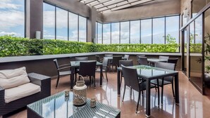 Un patio al aire libre con mesas y sillas de vidrio, un sofá y vistas a la vegetación.