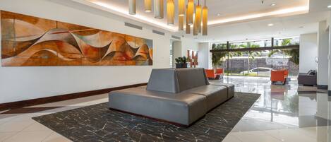 A modern lobby with a large abstract painting, a grey sofa, and a black marble rug.