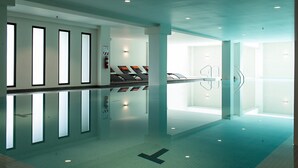Una piscina interior moderna con paredes de vidrio transparente, suelo de baldosas y diseño minimalista.