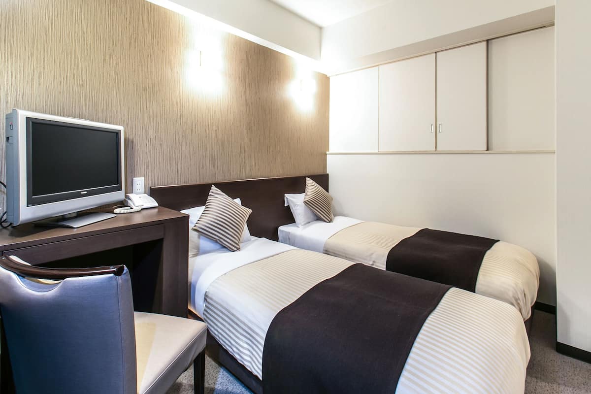Hotellihuone, jossa on kaksi sänkyä, työpöytä tietokoneella ja tuoli.