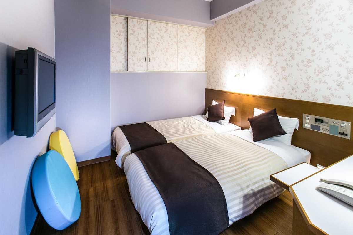 Hotellihuone, jossa on sänky, yöpöytä ja seinälle asennettu televisio.