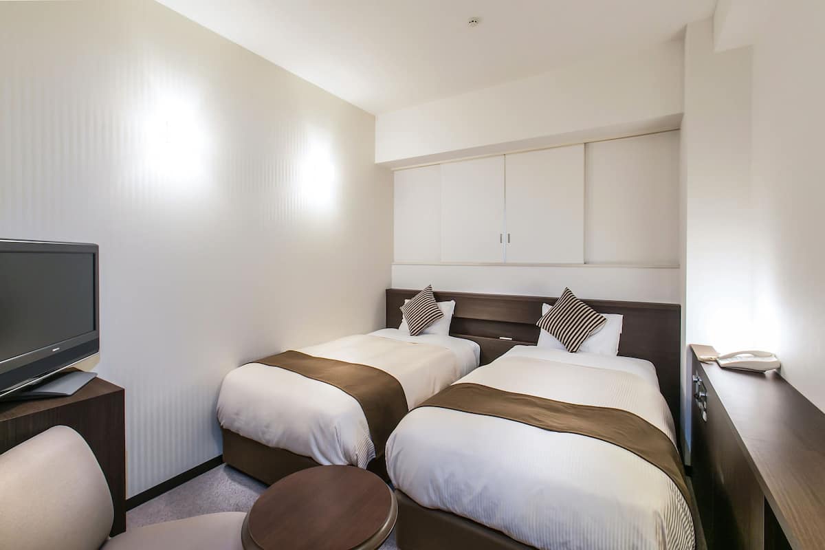 Hotellihuone, jossa on kaksi sänkyä, televisio, pieni pyöreä pöytä ja työpöytä, jossa on puhelin.