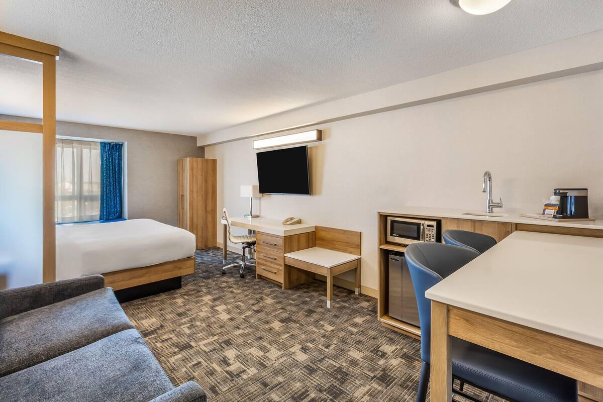 A hotel room with a bed, desk, chair, TV, and a microwave.