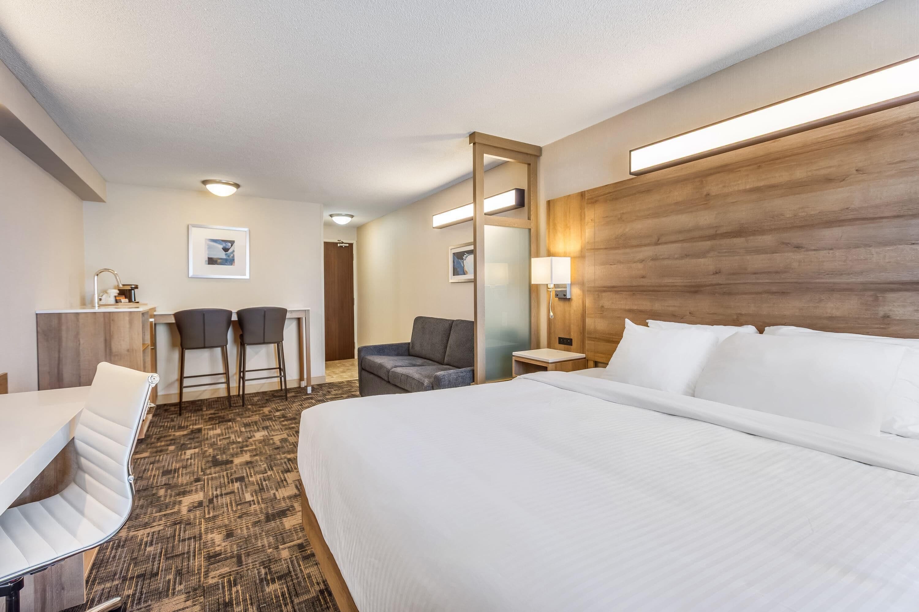 Une chambre d’hôtel avec un grand lit, un bureau avec deux chaises, une petite table et un miroir.