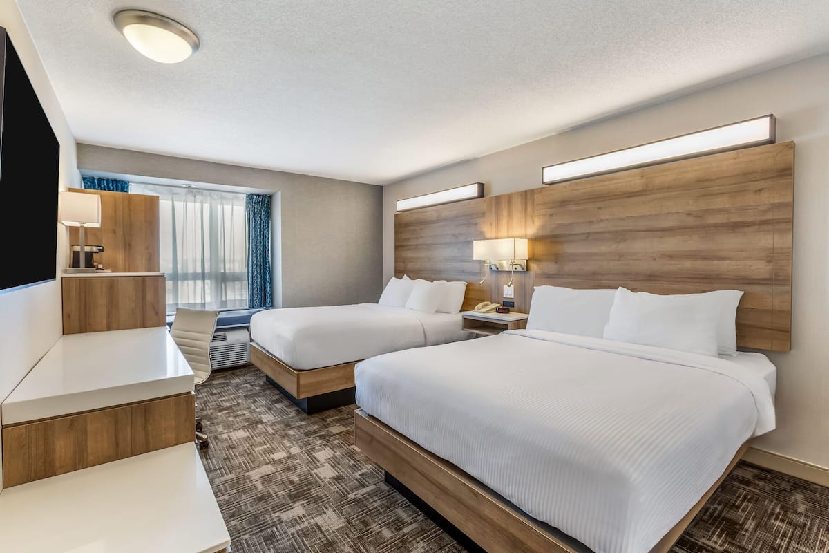 A hotel room with two beds, a desk, a lamp, and a window with curtains.