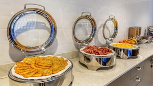 Un buffet proposant une variété de plats présentés dans des récipients en métal, un mur recouvert de carreaux et un comptoir en marbre.