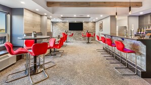 A modern bar area with red chairs, a stone wall, and a flat-screen TV.