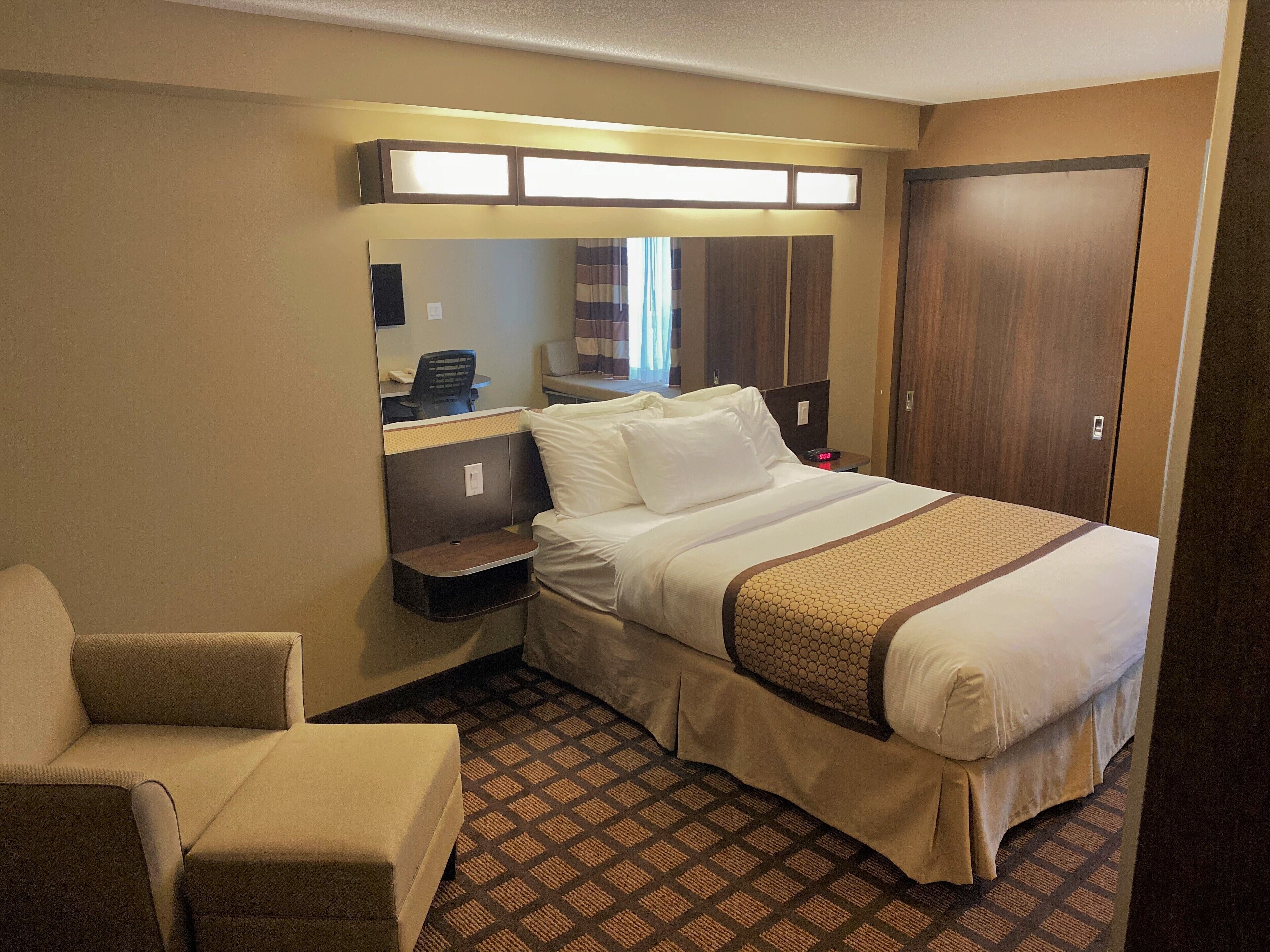 Una habitación de hotel con una cama, una silla, un escritorio y un espejo.