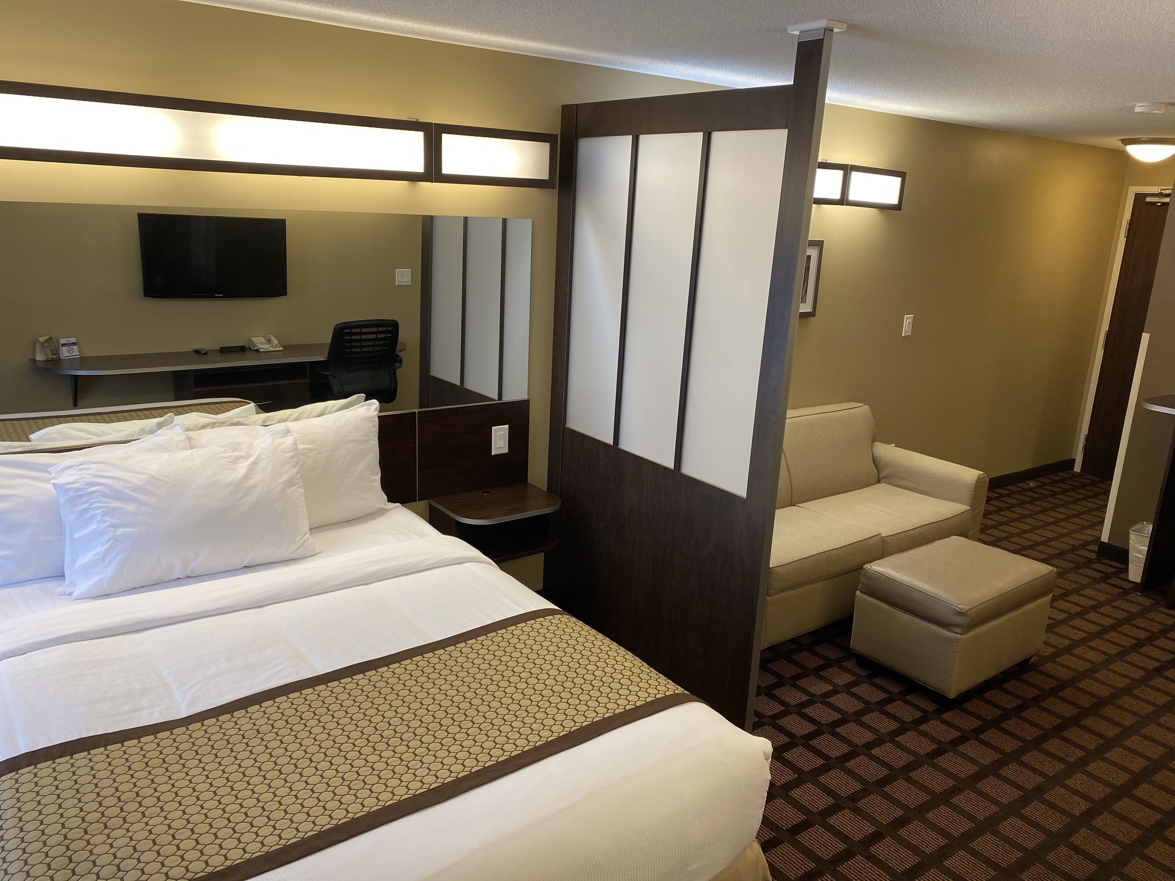 A hotel room with a large bed, a desk with a chair, a sofa, and a television.