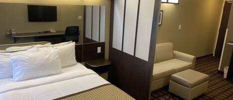 A hotel room with a large bed, a desk with a chair, a sofa, and a television.