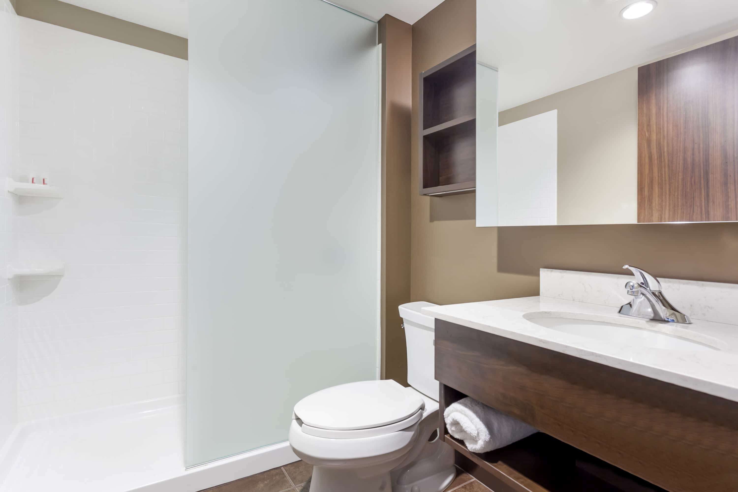 Un baño moderno con cabina de ducha de vidrio, inodoro blanco y tocador de madera con lavamanos.
