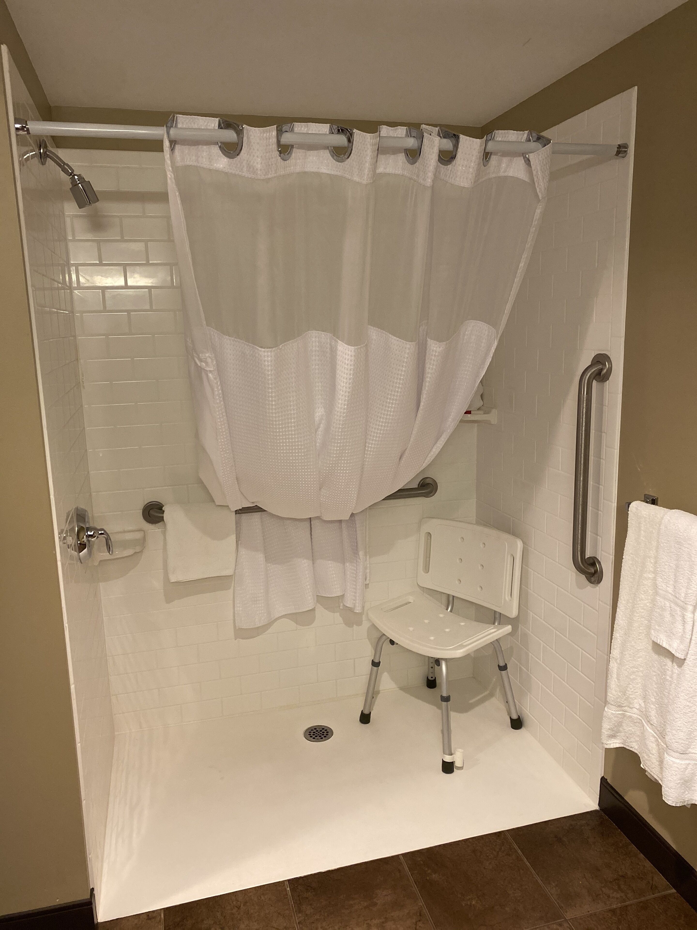 Una ducha a nivel del suelo con una cortina blanca, una toalla blanca y una silla blanca.