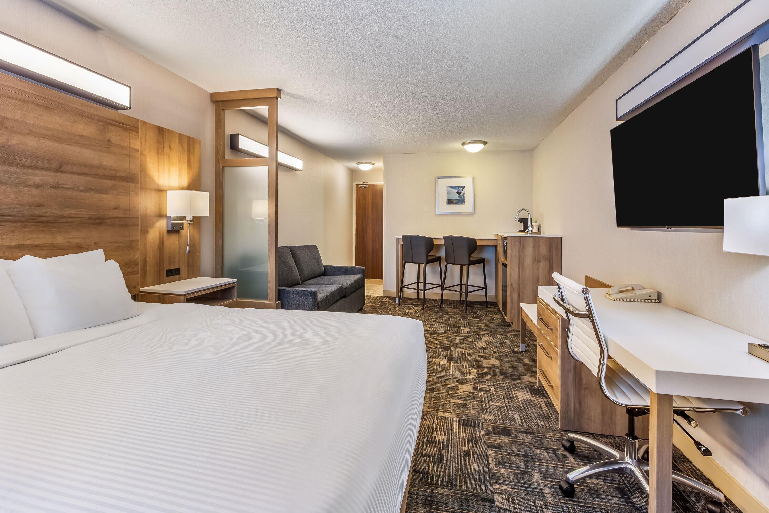 A hotel room with a large bed, a desk with a chair, a TV, and a desk lamp.