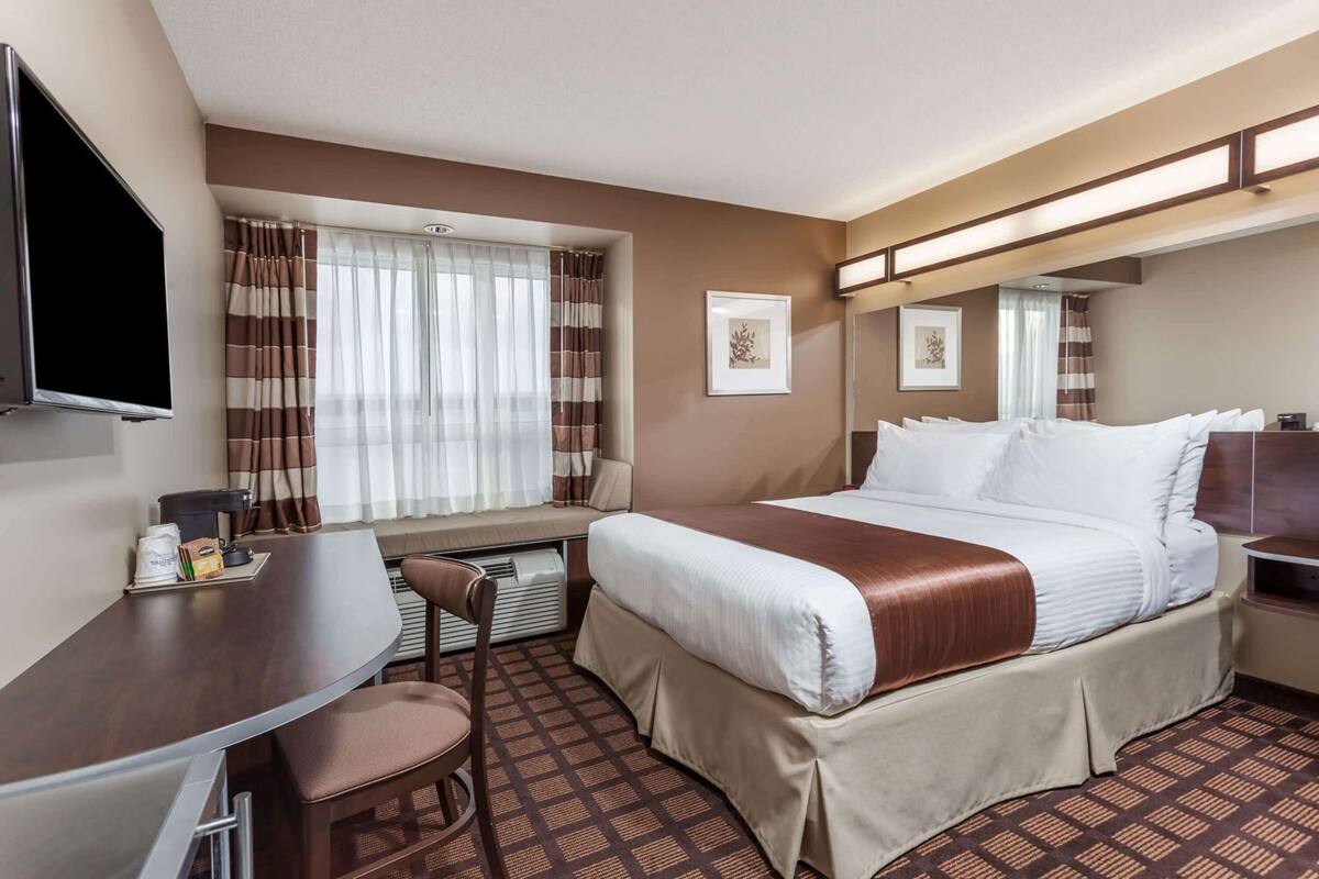 A hotel room with a bed, a desk, a chair, a TV, and a window with curtains.