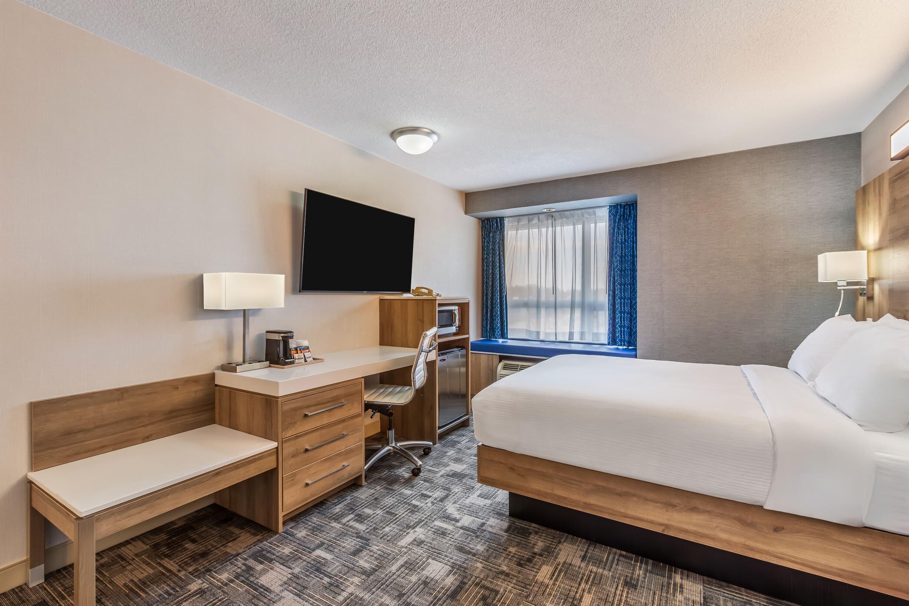 A hotel room with a bed, desk, chair, television, and a window with curtains.