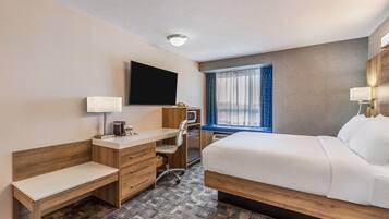 A hotel room with a bed, desk, chair, television, and a window with curtains.