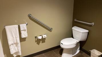 A bathroom with a white toilet, two handrails, a trash bin, and two towels on a rack.