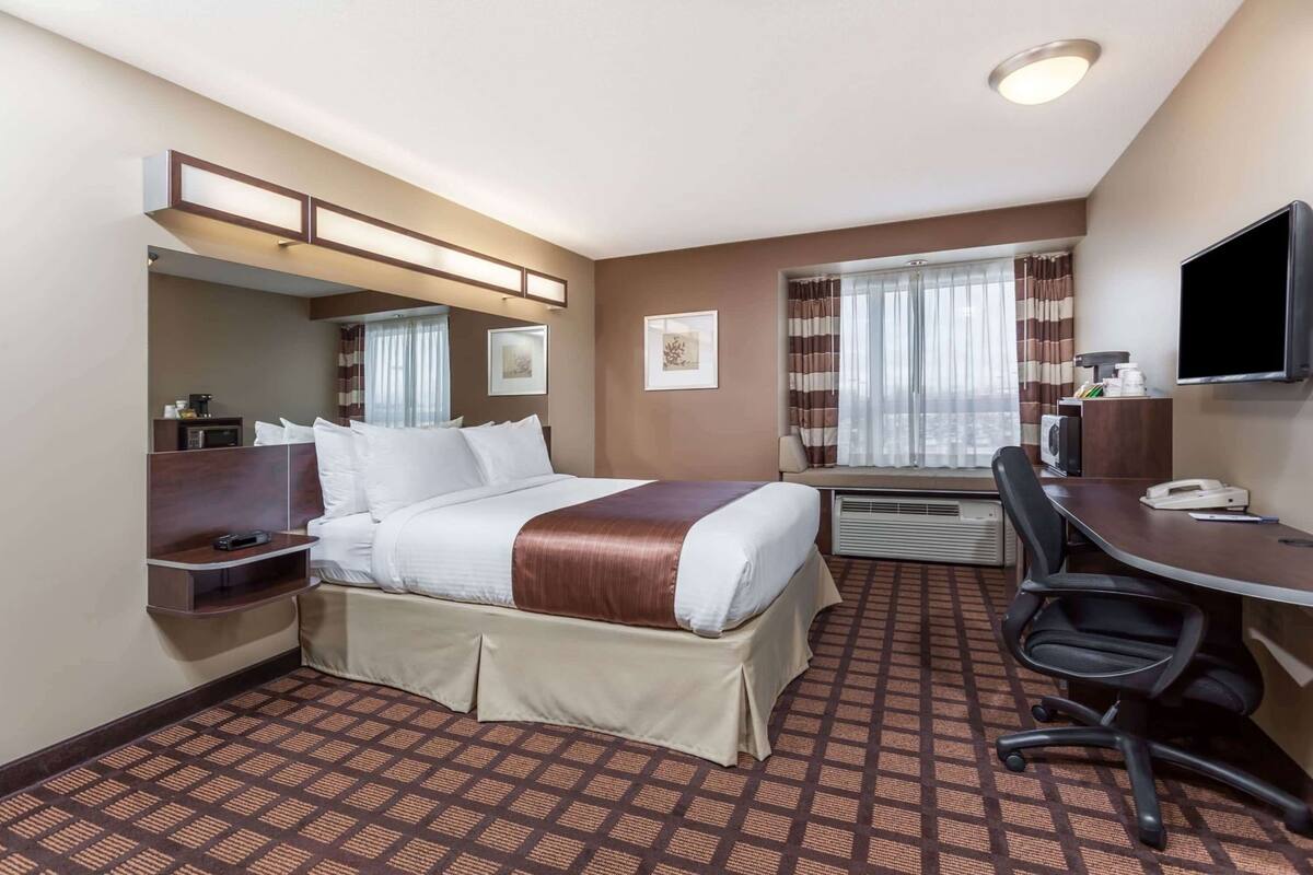 A hotel room with a bed, desk, chair, TV, and a window with curtains.