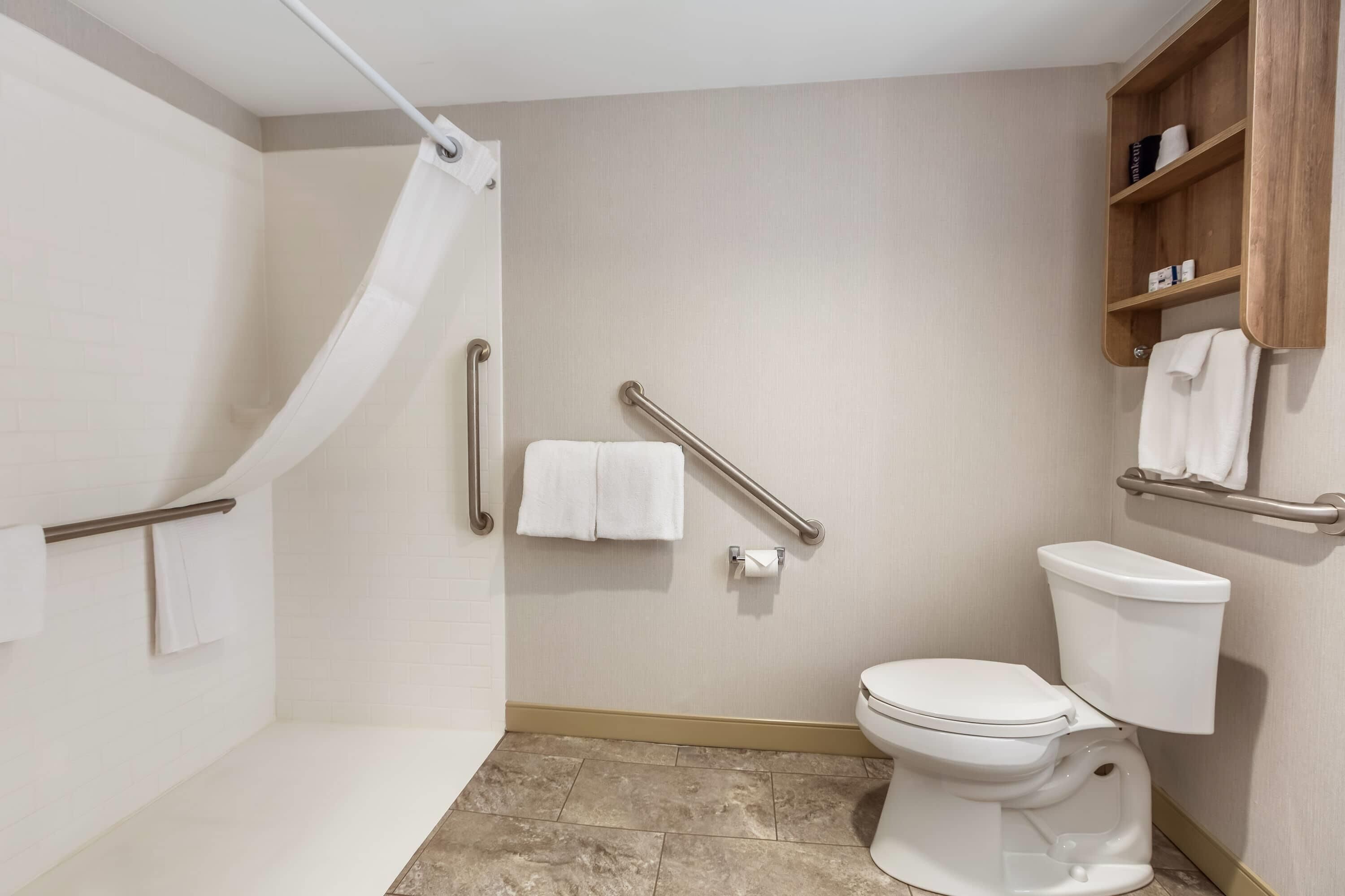 A bathroom with a shower, toilet, grab bars, and a towel rack.
