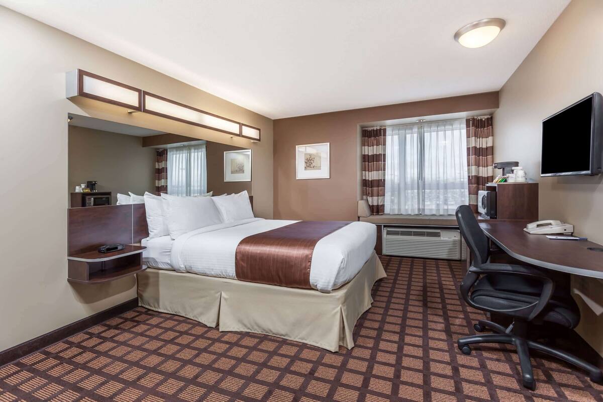 A hotel room with a bed, desk, chair, and a television.