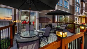 Une terrasse avec des sièges extérieurs, une porte vitrée donnant sur un espace intérieur et un bâtiment doté de nombreuses fenêtres.