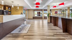 Un espace d’accueil d’hôtel avec un plancher en bois, un comptoir de réception, une horloge et une machine à café.