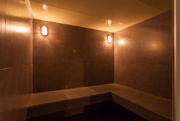 A modern bathroom with dark tiles, recessed lighting, and a bench.