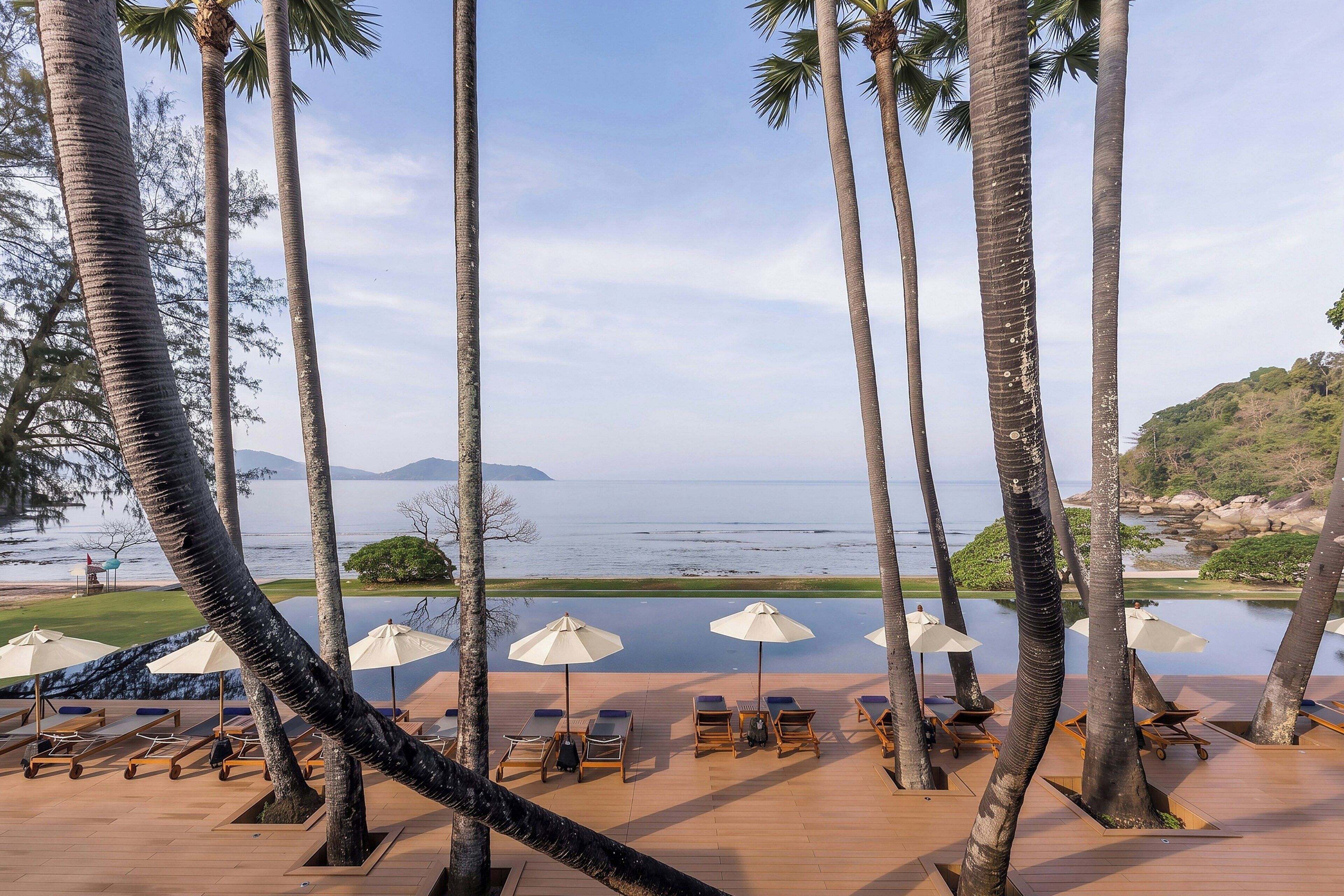 A poolside area with lounge chairs and umbrellas, overlooking a body of water and greenery.