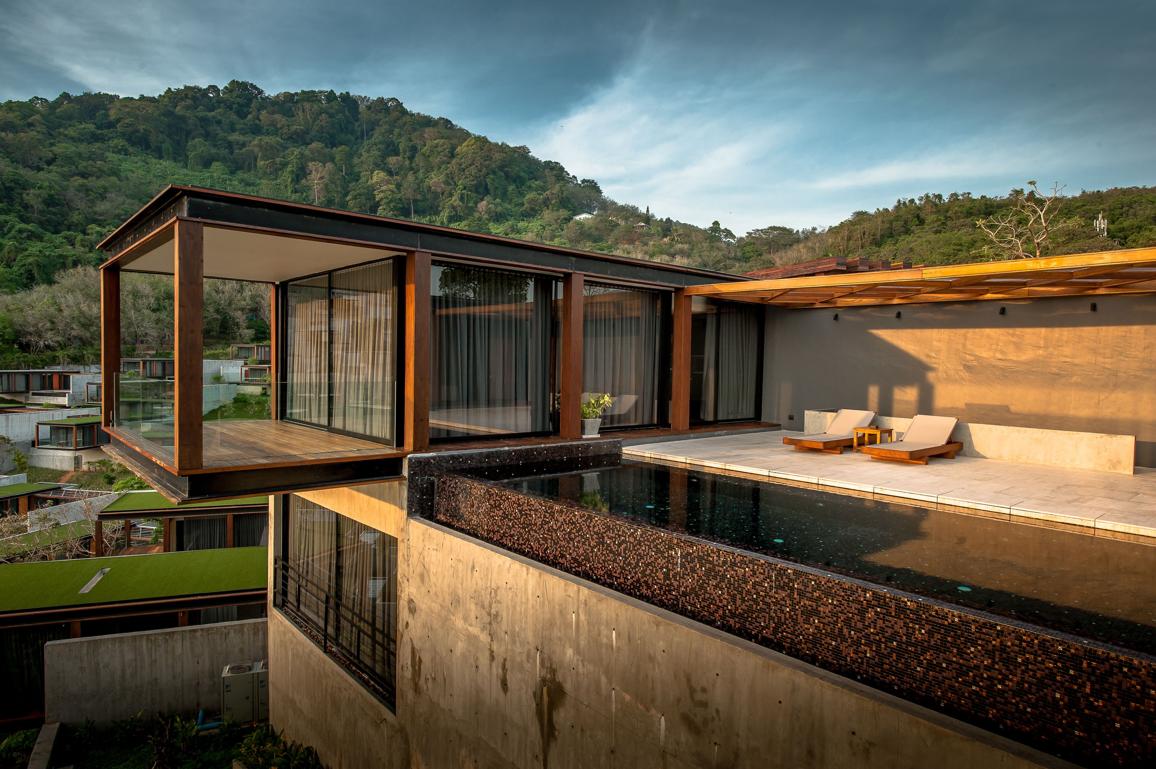 A modern outdoor pool area with a glass-enclosed lounge and a view of a forested hillside.