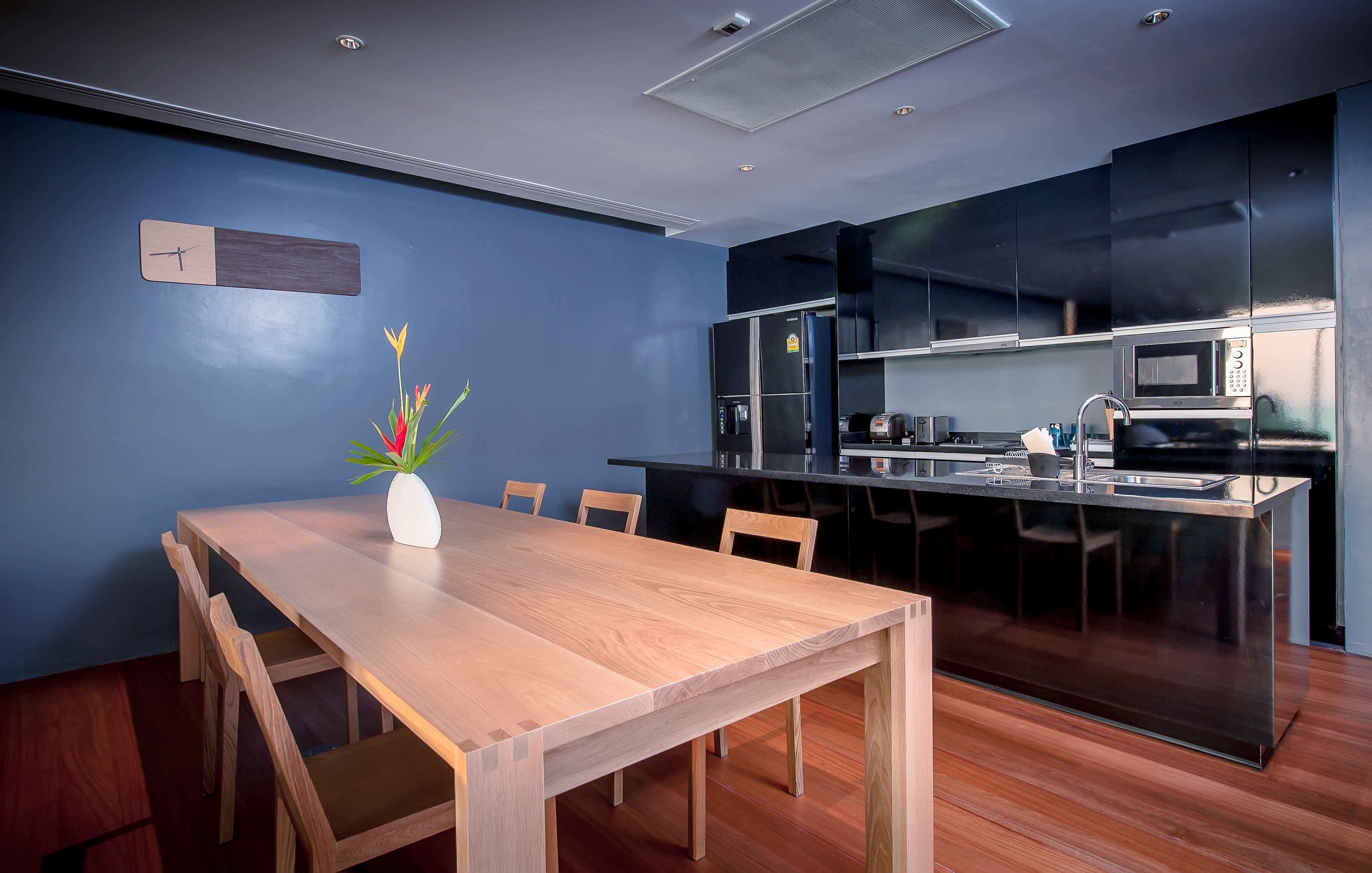 A modern kitchen with a wooden dining table and chairs, a built-in microwave, and a stainless steel sink.
