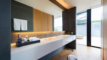 A modern bathroom with a long white sink, wooden cabinets, and a large mirror.