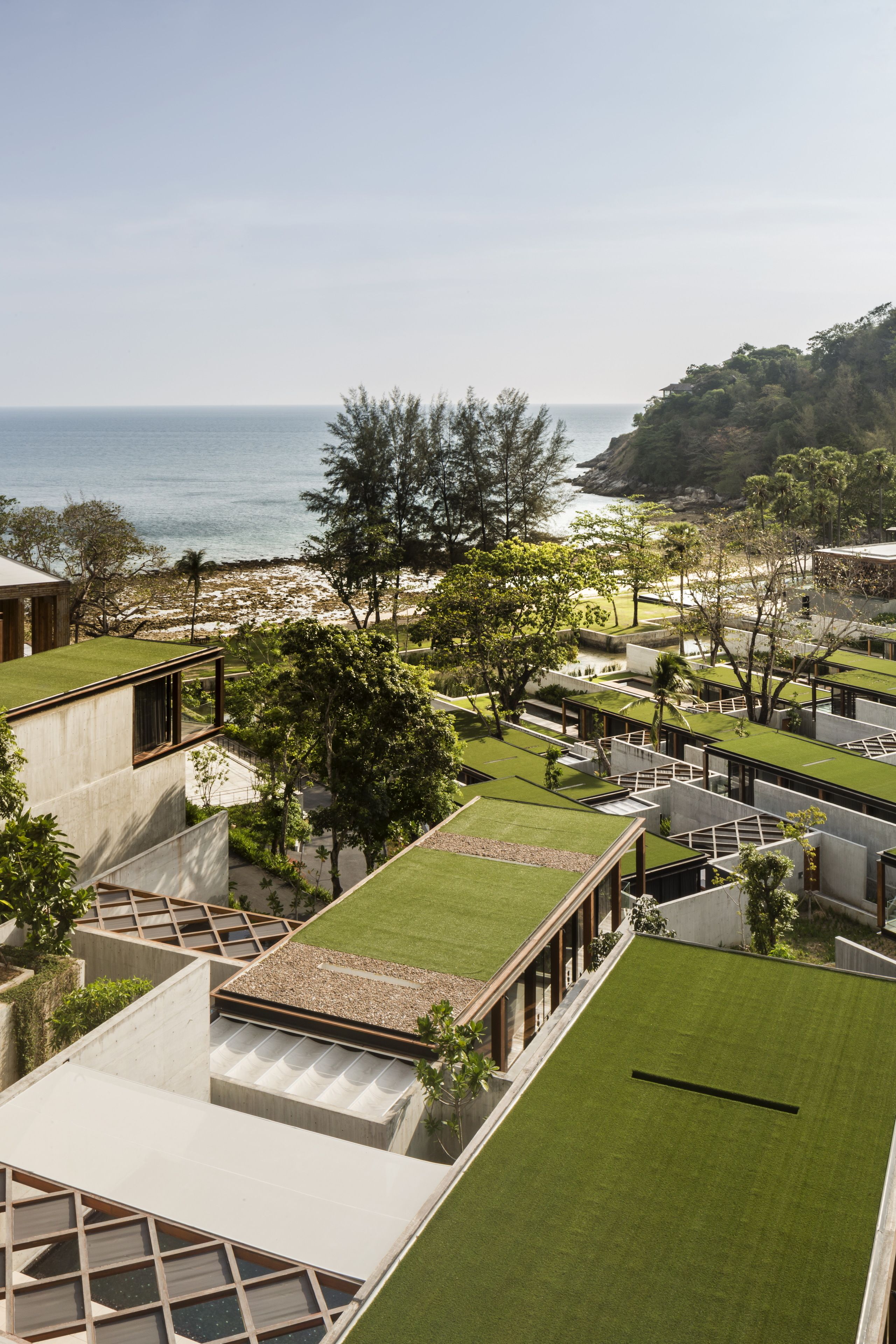 Hotel moderno com jardins no terraço, vista para o mar e paisagem montanhosa ao fundo.