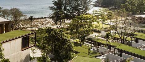 A modern hotel with rooftop gardens, a view of the sea, and a hilly landscape in the background.