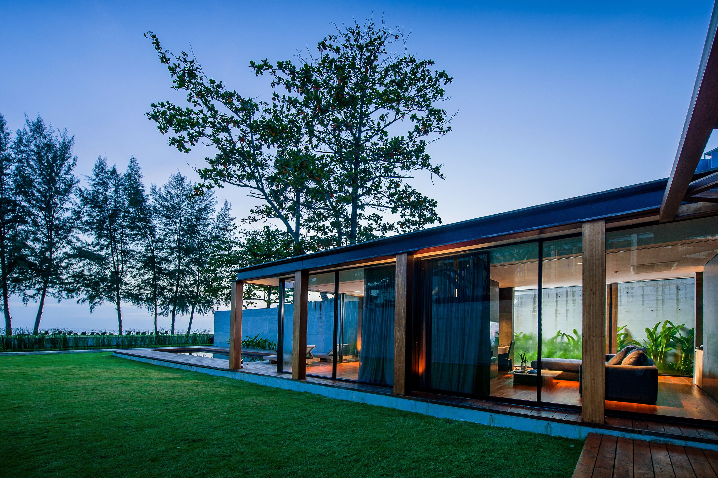 A modern house with large glass windows, a wooden deck, and a view of the sea.